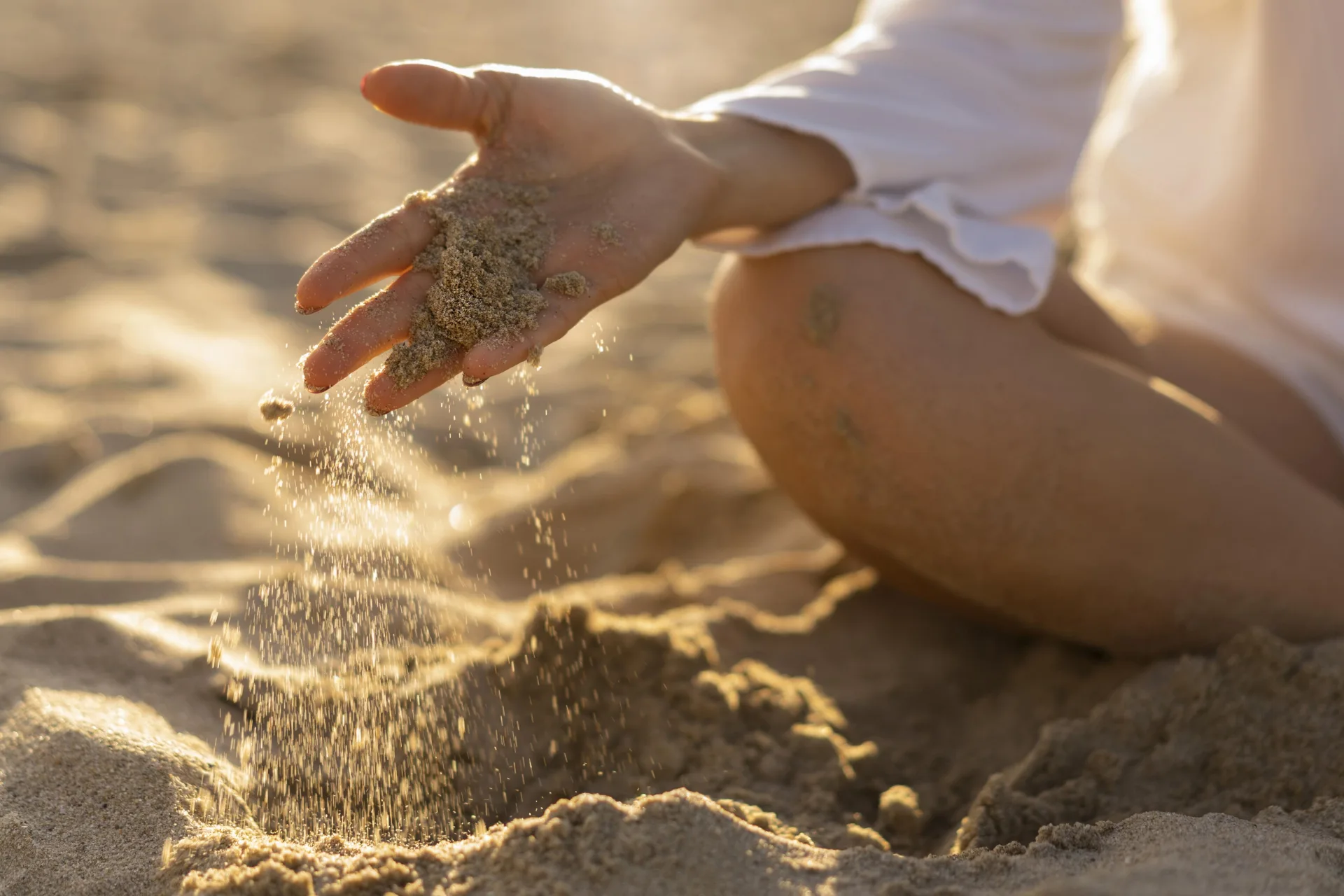 Una mano lascia scivolare la sabbia fra le dita, su una spiaggia nella luce del tramonto